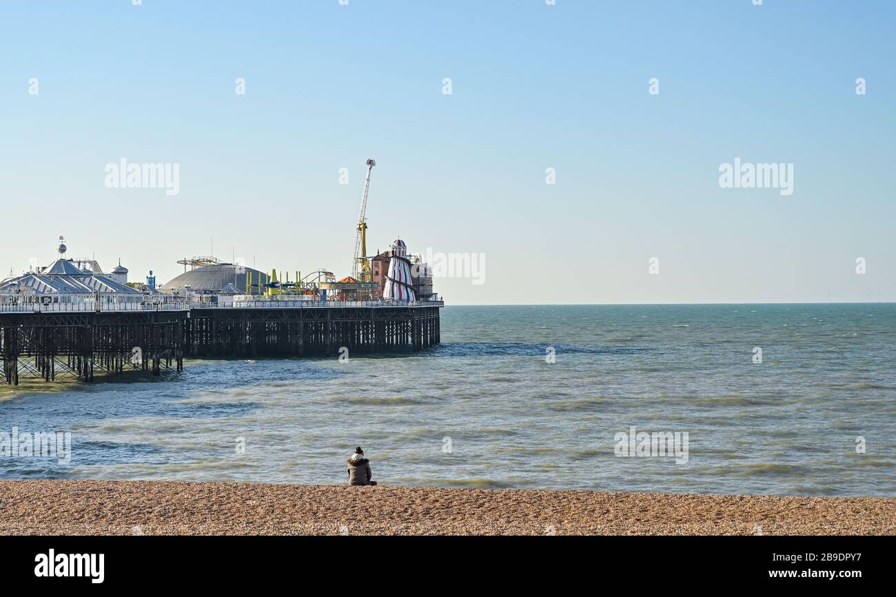 Brighton UK 24 Marzo 2020 - UNA persona siede da sola sulla spiaggia di Brighton in una bella mattinata di sole come le nuove restrizioni del governo entrano durante la crisi pandemica Coronavirus COVID-19 . Credit: Simon Dack / Alamy Live News Foto Stock