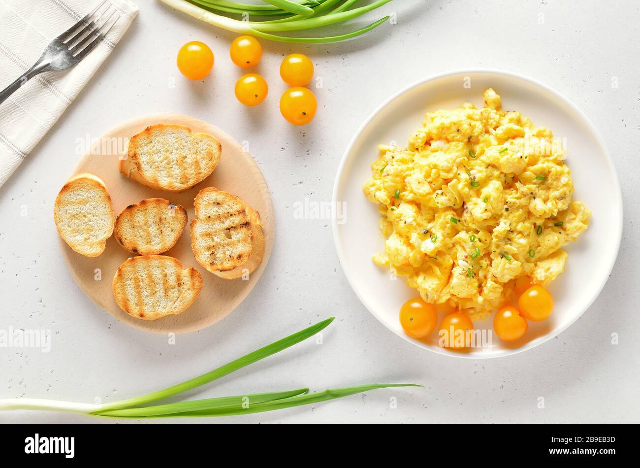 Uova strapazzate e pomodori sul piatto su fondo di pietra chiaro. Vista dall'alto, disposizione piatta Foto Stock