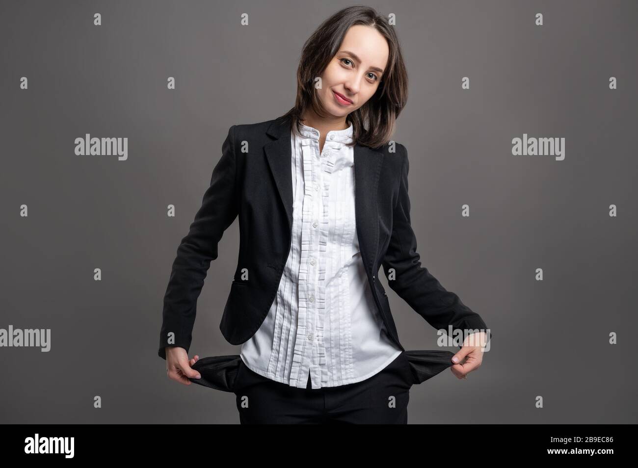 Ritratto di donna giovane e meravigliosa business wering nero vestito e camicia mostrando tasche vuote che si posano su isolato sfondo grigio Foto Stock
