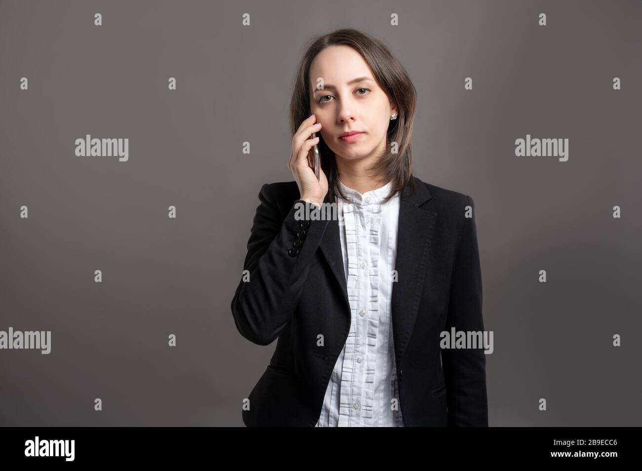 Ritratto di donna giovane e meravigliosa business wering nero vestito e camicia che parla sul cellulare posando su sfondo grigio isolato Foto Stock