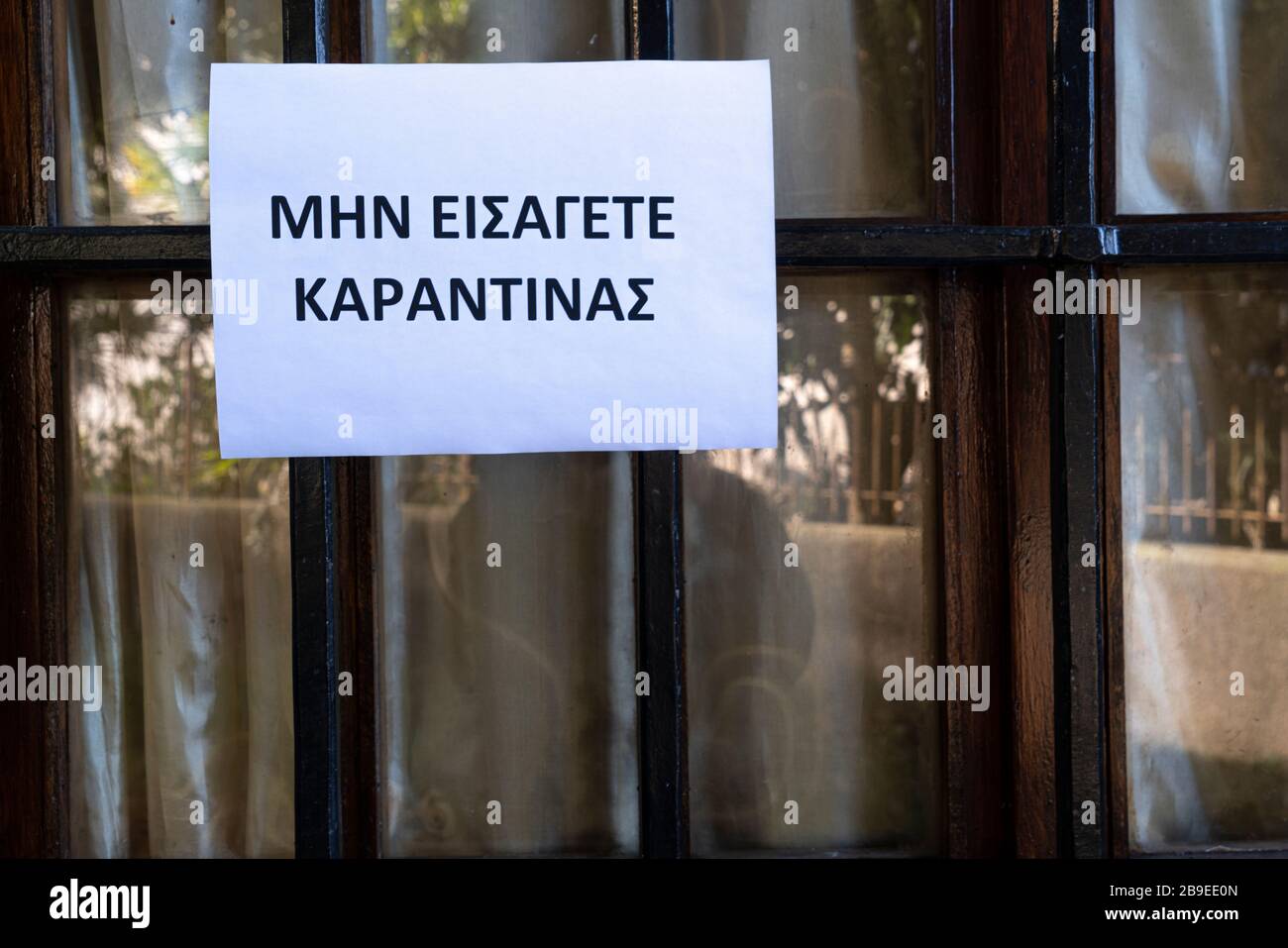 Un segno che dice non entrare, quarantena in lingua greca allegato su una finestra Foto Stock