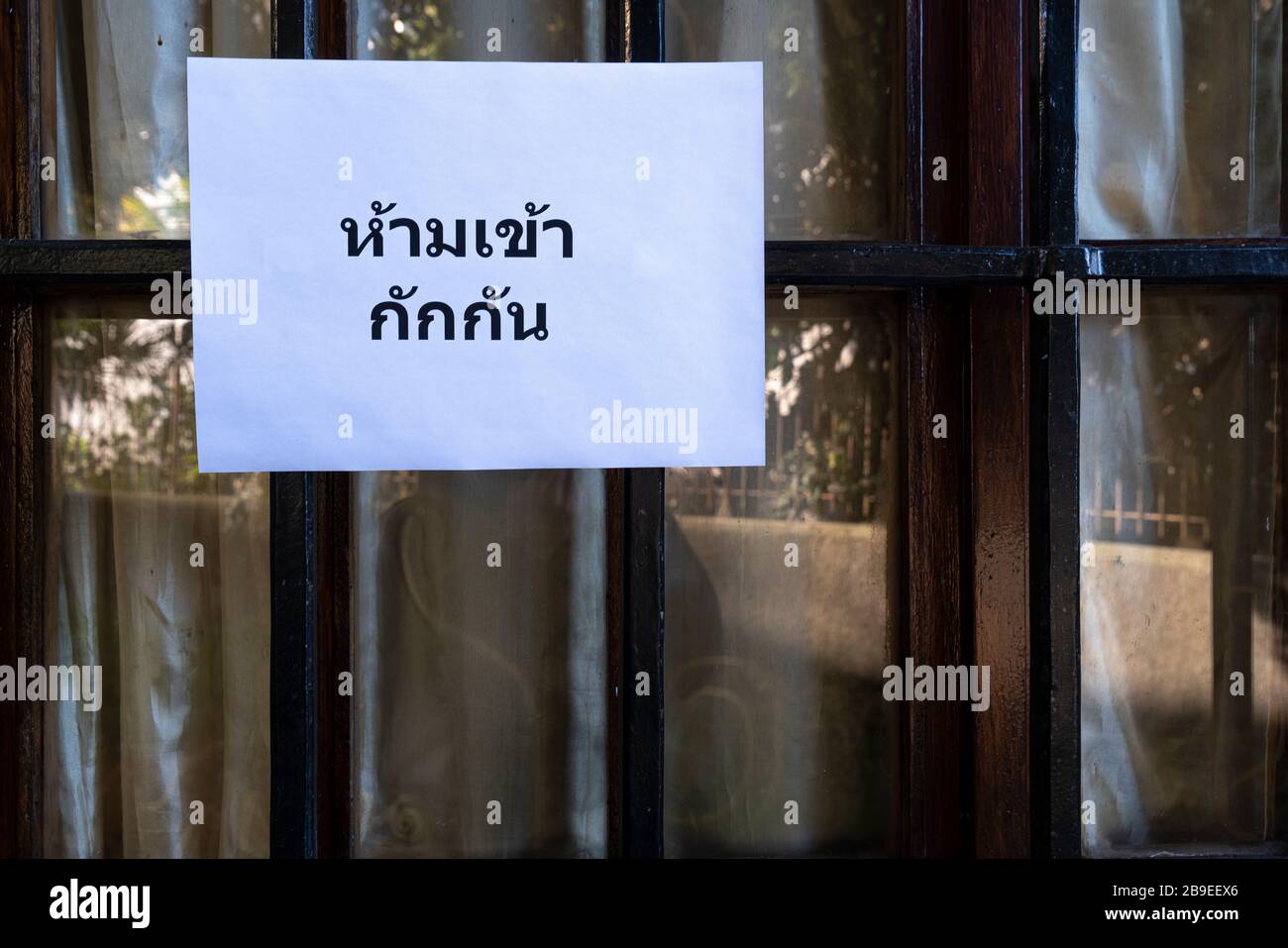 Un segno che dice non entrare, quarantena in lingua tailandese allegato su una finestra Foto Stock