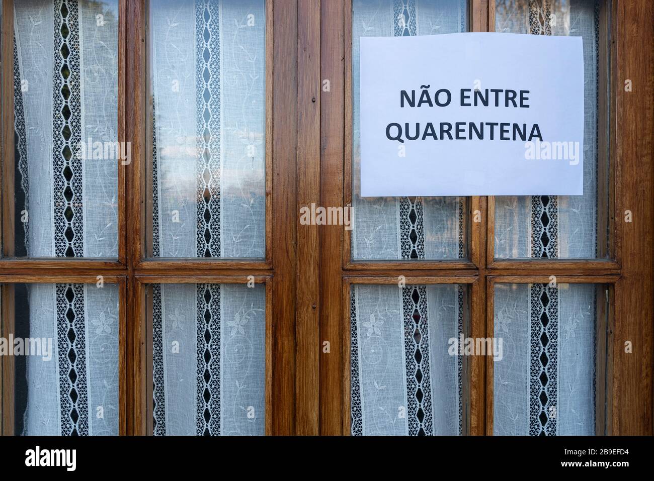 Un segno che dice non entrare, quarantena in lingua portoghese allegato su una finestra Foto Stock