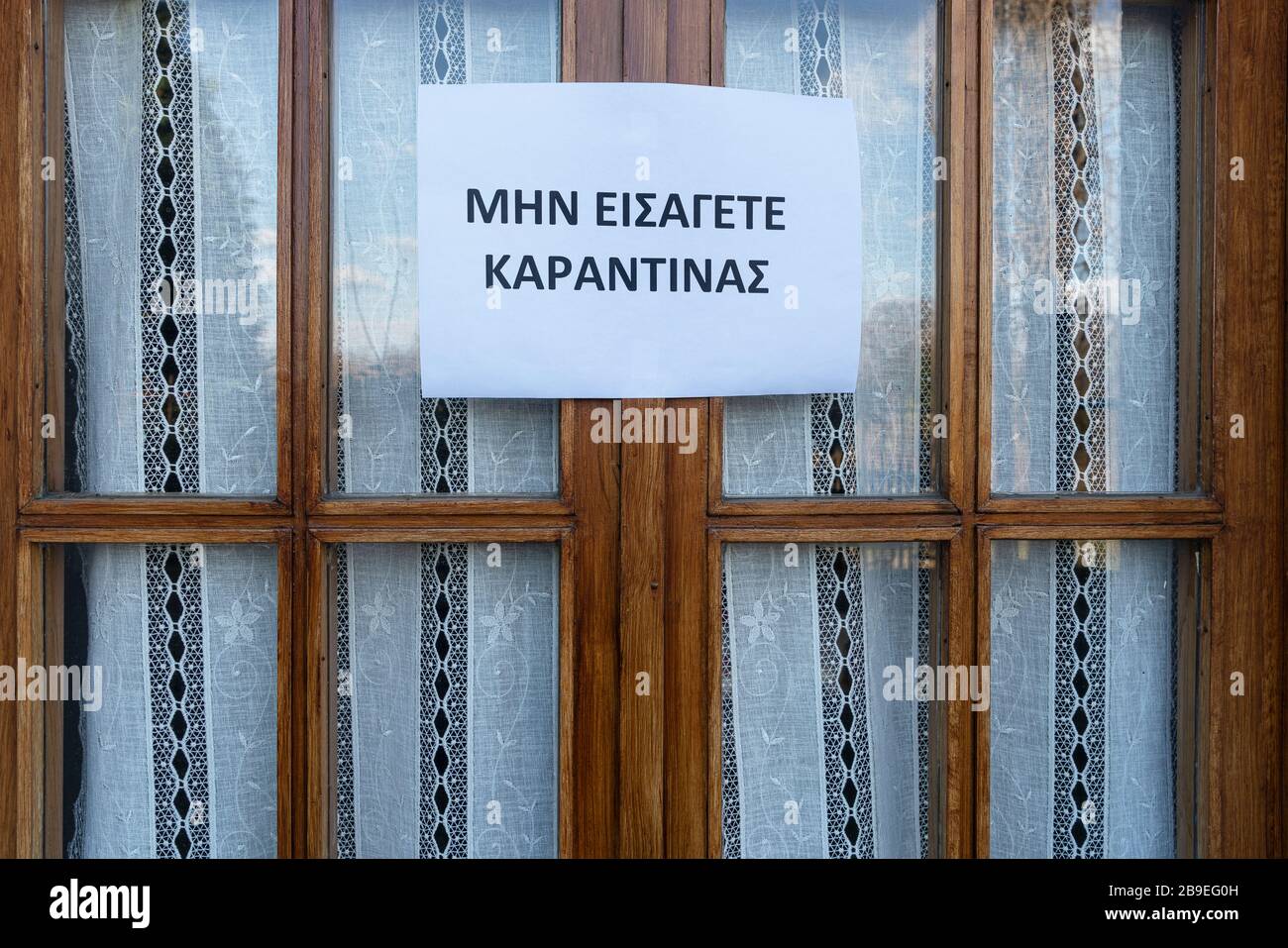 Un segno che dice non entrare, quarantena in lingua greca allegato su una finestra Foto Stock