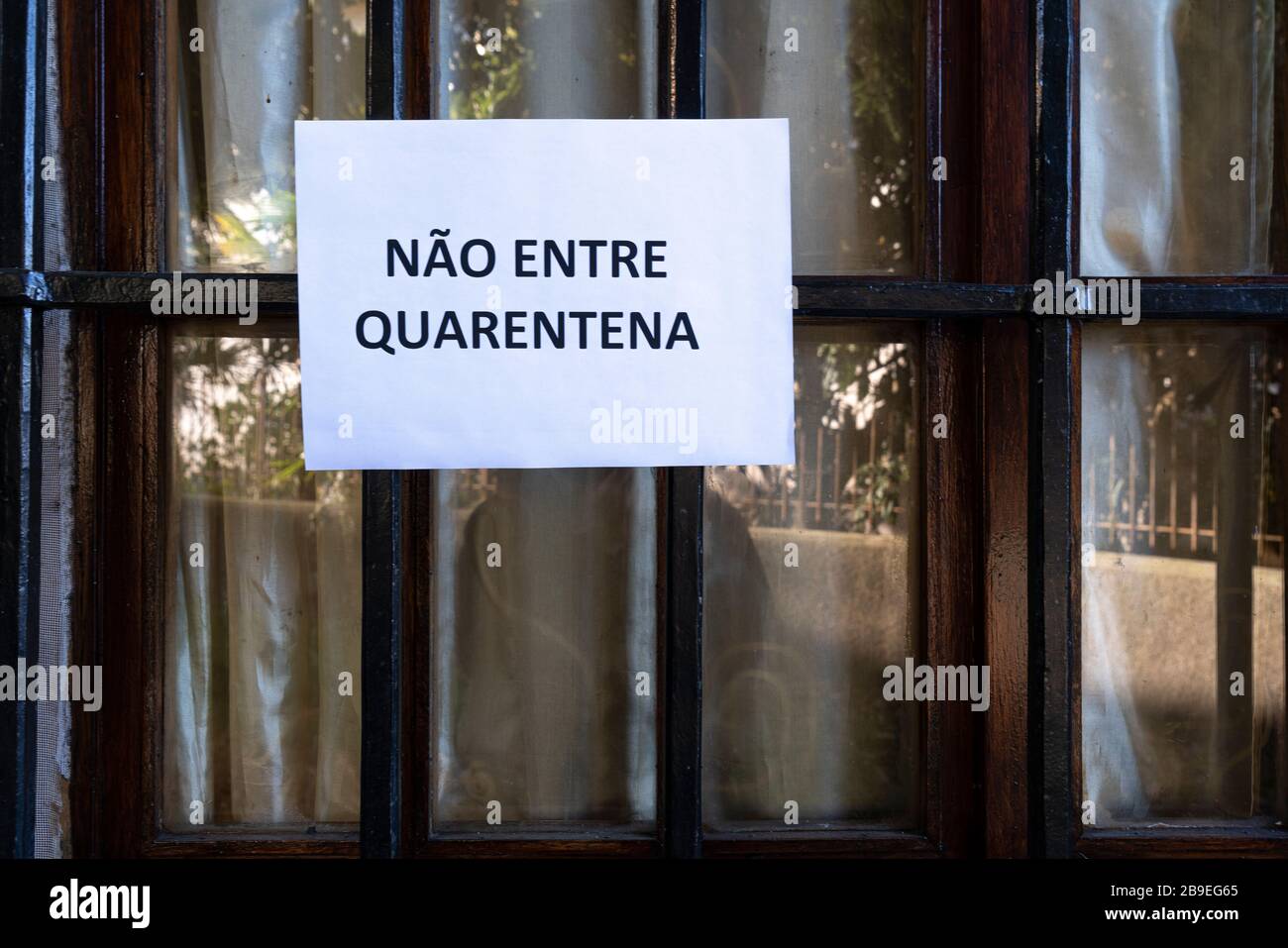 Un segno che dice non entrare, quarantena in lingua portoghese allegato su una finestra Foto Stock