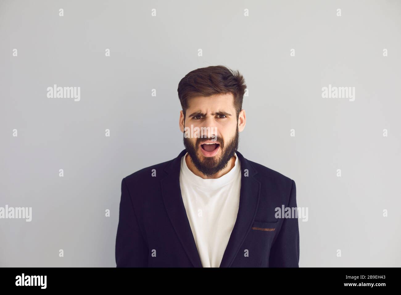 La bruna etnica maschile con emozione negativa ha un problema di stress su uno sfondo grigio. Foto Stock