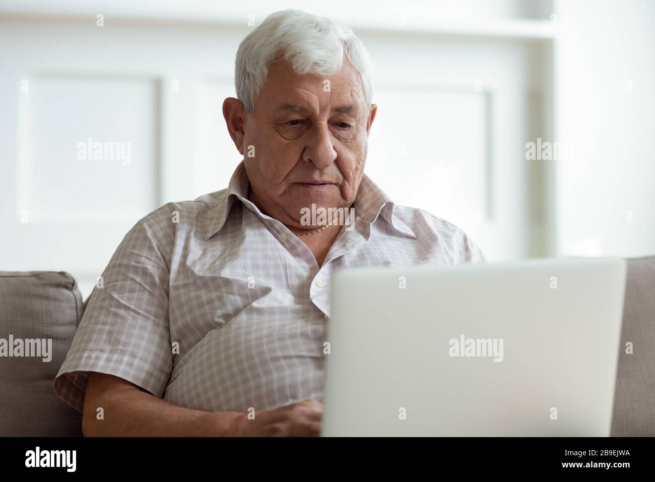 Uomo anziano serio che usa il laptop primo piano, guardando lo schermo Foto Stock