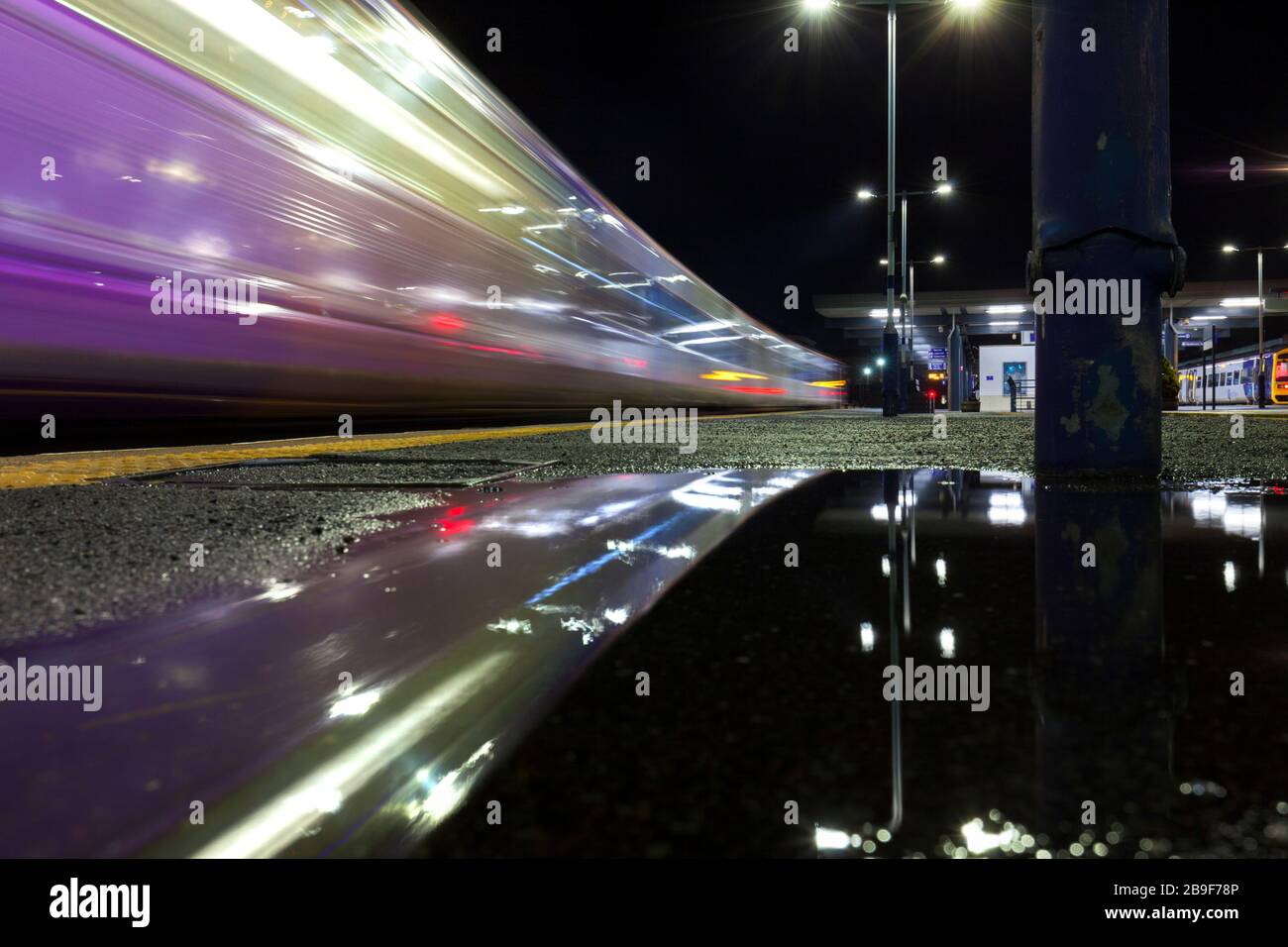 Northern Rail classe 142 treno di pacer in partenza dalla stazione ferroviaria di Blackburn riflesso in una pozzanghera sulla piattaforma della stazione con movimento sfocato Foto Stock