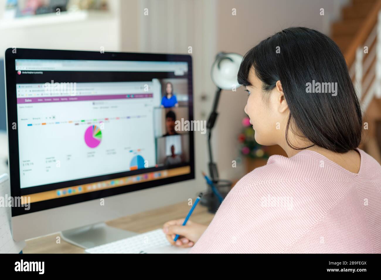 Vista posteriore della donna asiatica d'affari che parla con i suoi colleghi circa il programma nella video conferenza. Un team aziendale multietnico che utilizza il computer per un incontro online Foto Stock