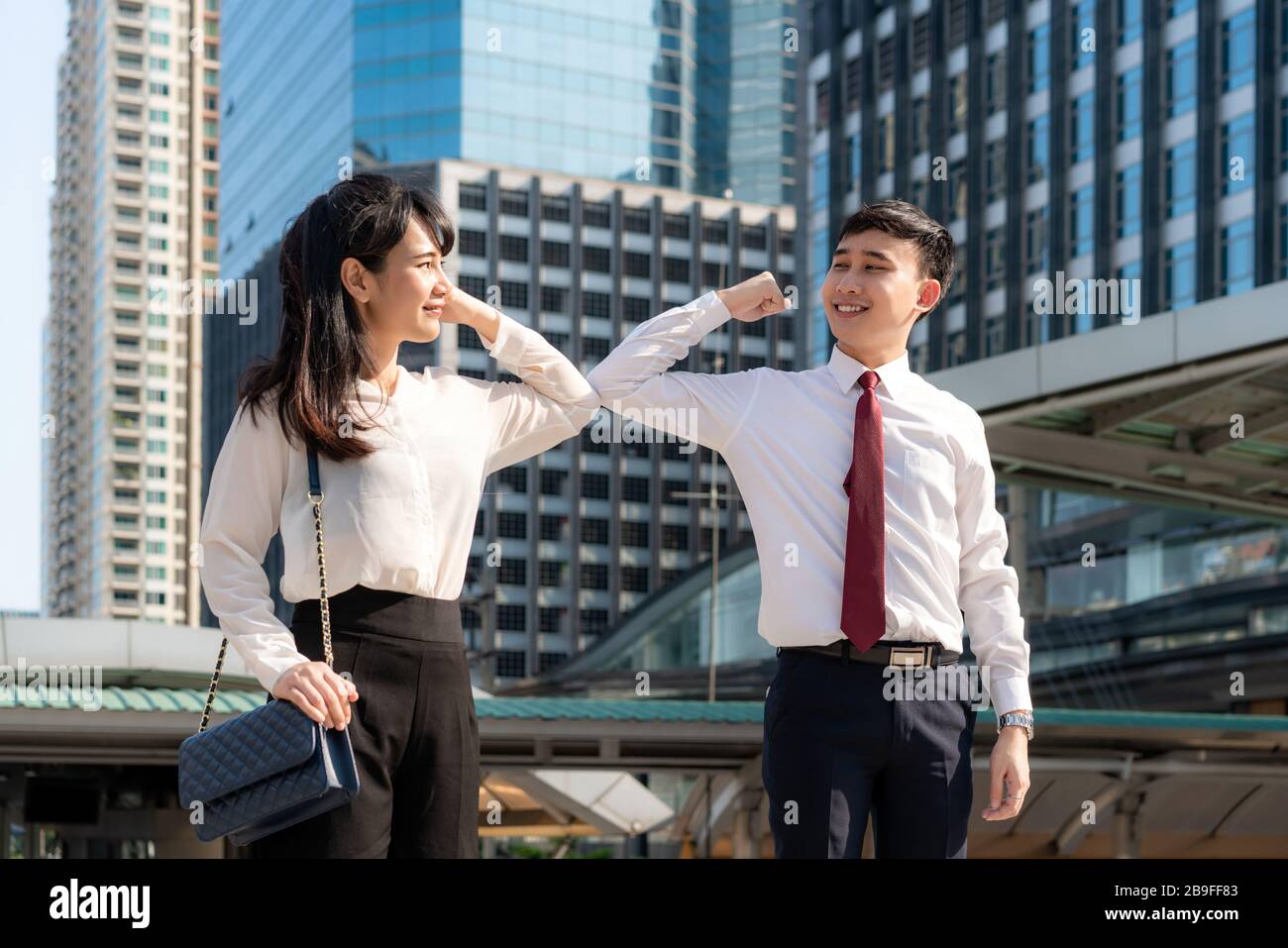 Gomito bump è nuovo saluto per evitare la diffusione di coronavirus. Due amici d'affari asiatici si incontrano di fronte all'edificio degli uffici. Invece di salutare Foto Stock