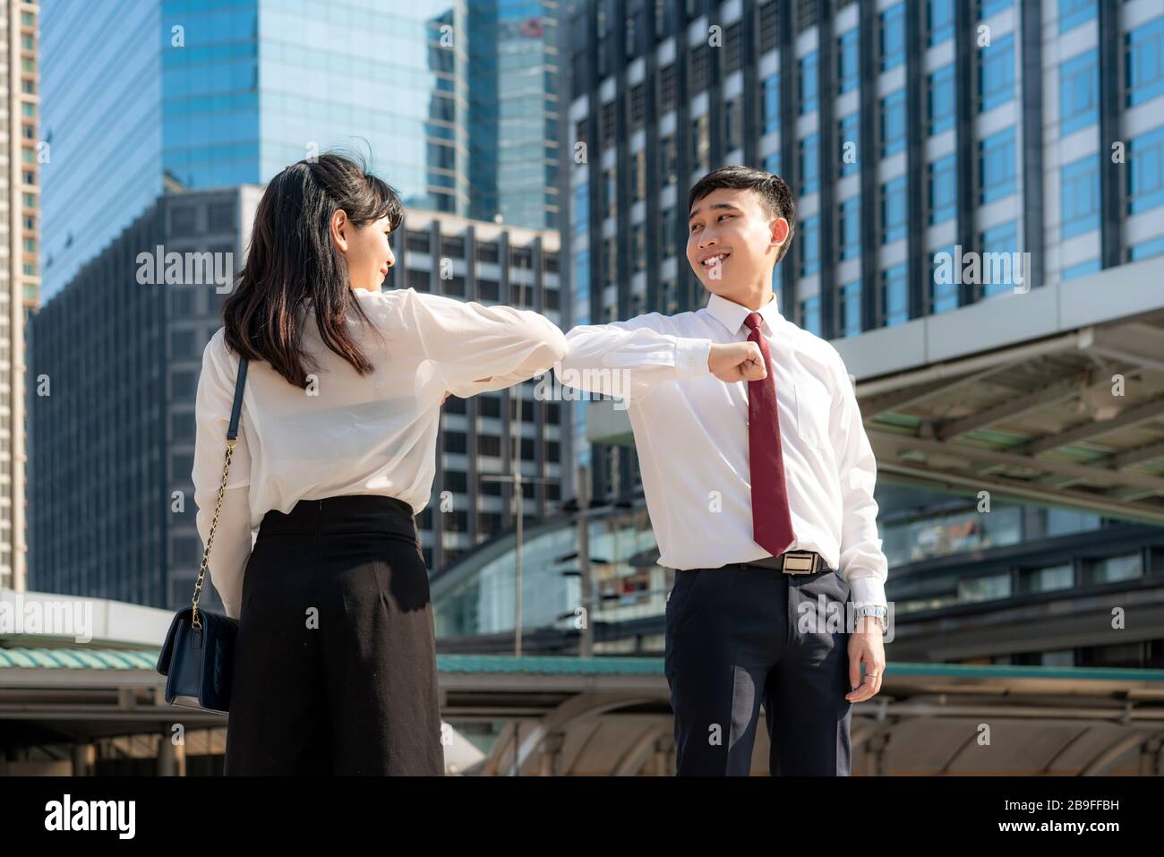 Gomito bump è nuovo saluto per evitare la diffusione di coronavirus. Due amici d'affari asiatici si incontrano di fronte all'edificio degli uffici. Invece di salutare Foto Stock