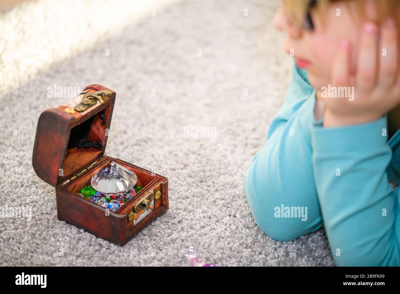 Primo piano di un ragazzo di cinque anni ammirando un tesoro pieno di gemme multicolore. Ha allineato le gemme sul pavimento. Foto Stock