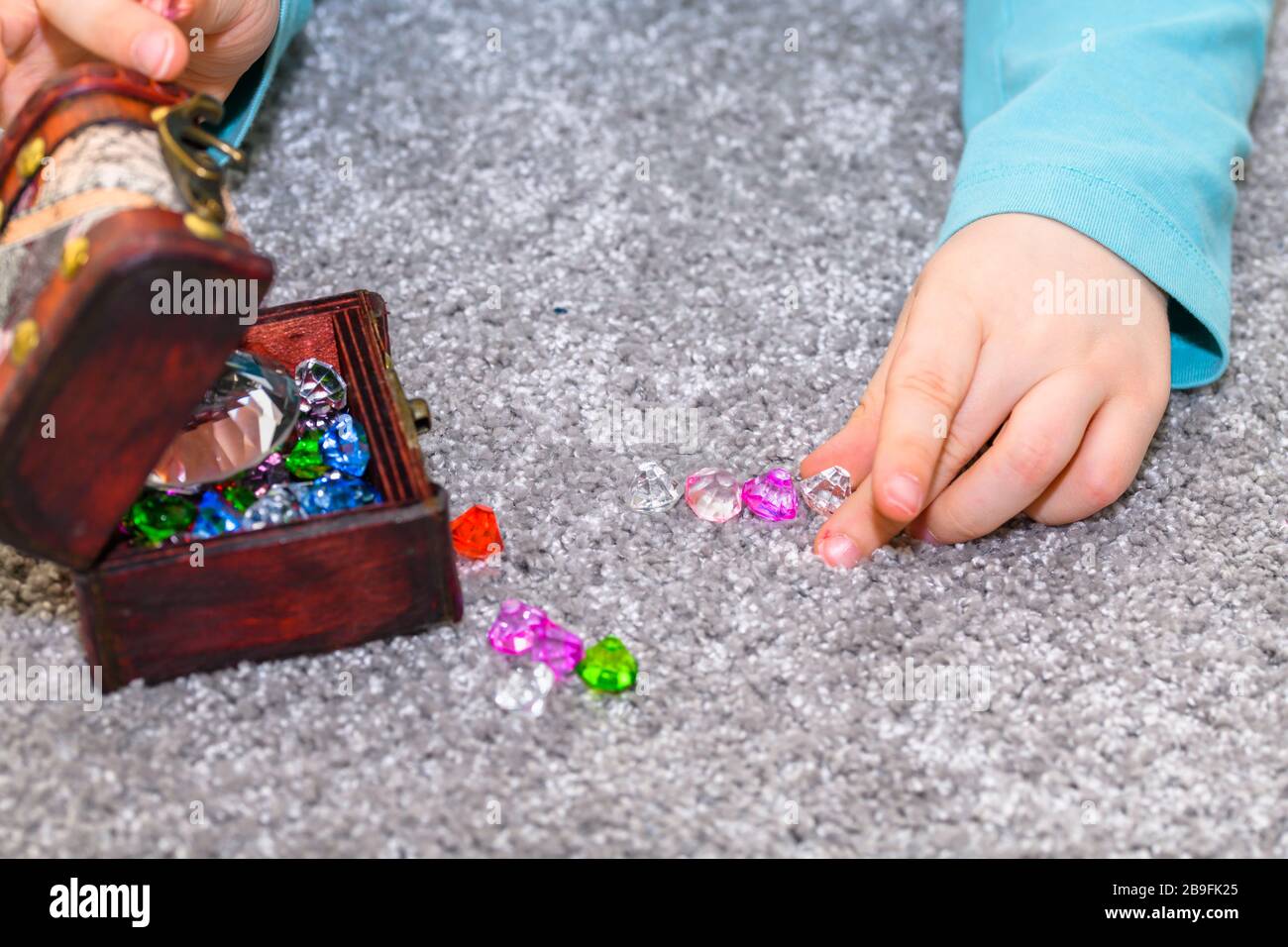 Ragazzo di cinque anni con una cassa del tesoro piena di gemme multicolori. Il ragazzo sta giocando e allineando le gemme. Foto Stock
