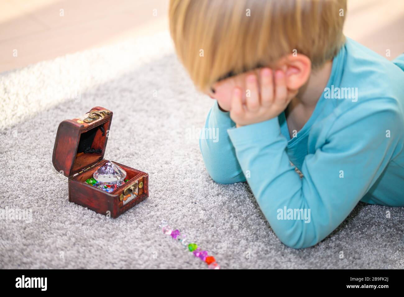 Ragazzo di cinque anni che ammirava un tesoro pieno di gemme multicolore. Ha allineato le gemme sul pavimento. Foto Stock