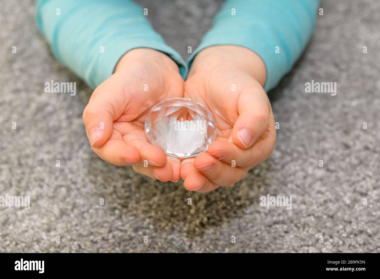 Primo piano delle mani a cubetti di un ragazzo di cinque anni che tiene un grande diamante di vetro. Il ragazzo ha una camicia turchese. Foto Stock