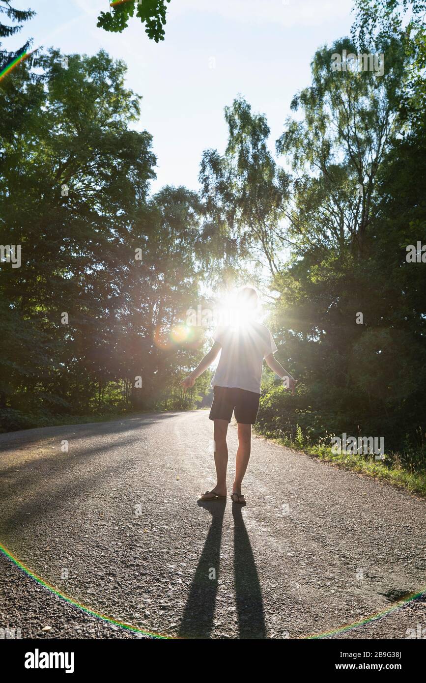 Uomo in piedi sotto gli alberi su strada soleggiata Foto Stock