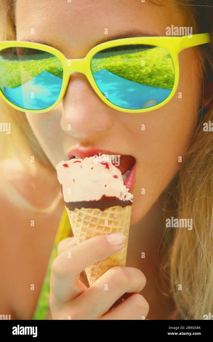 Primo piano ritratto giovane donna in occhiali da sole mangiare cono gelato Foto Stock