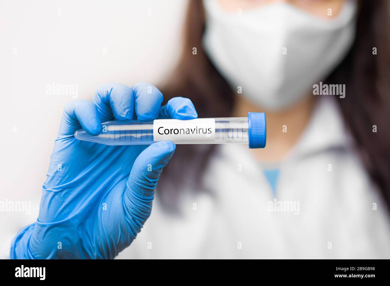 Provetta con vaccino contro il coronavirus, 2019-nCoV, SARS-nCov, COVID-19 in maschera protettiva e guanti blu per scienziato. Foto Stock