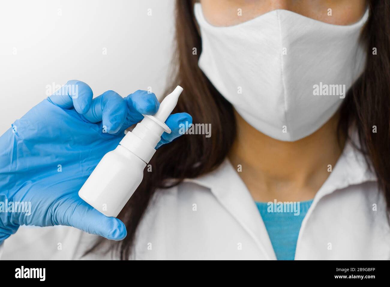 Una donna che usa spray nasale per il trattamento dell'influenza o il naso che corre tiene il medicinale in mano. Il medico in maschera protettiva e guanti blu mostra spray nasale per Foto Stock