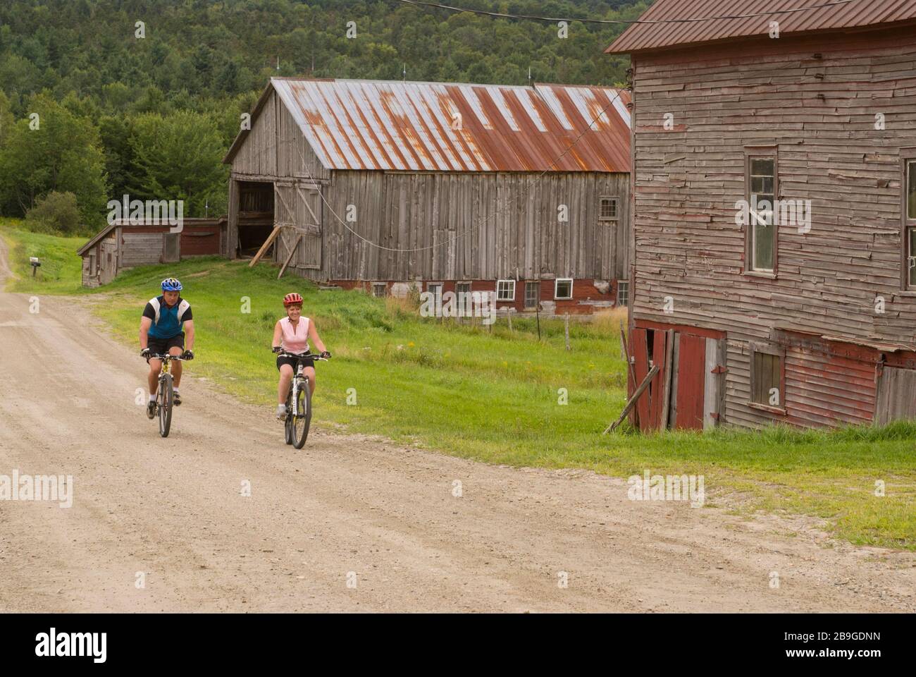 Coppia in mountain bike su una strada rurale e sterrata che passa fienili stagionato a Warren, Vermont, in una giornata estiva. Foto Stock