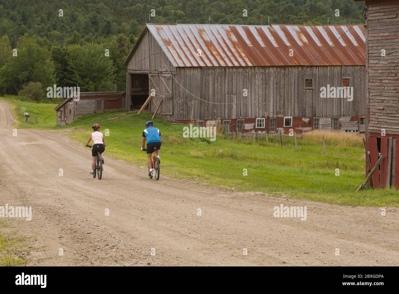 Coppia in mountain bike su una strada rurale e sterrata che passa fienili stagionato a Warren, Vermont, in una giornata estiva. Foto Stock