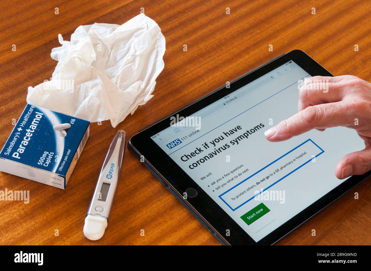 Una donna che utilizza un ipad per controllare il sito web NHS per consigli sui simpton Coronavirus Covid-19. Con paracetamolo, tessuto e termometro. Foto Stock