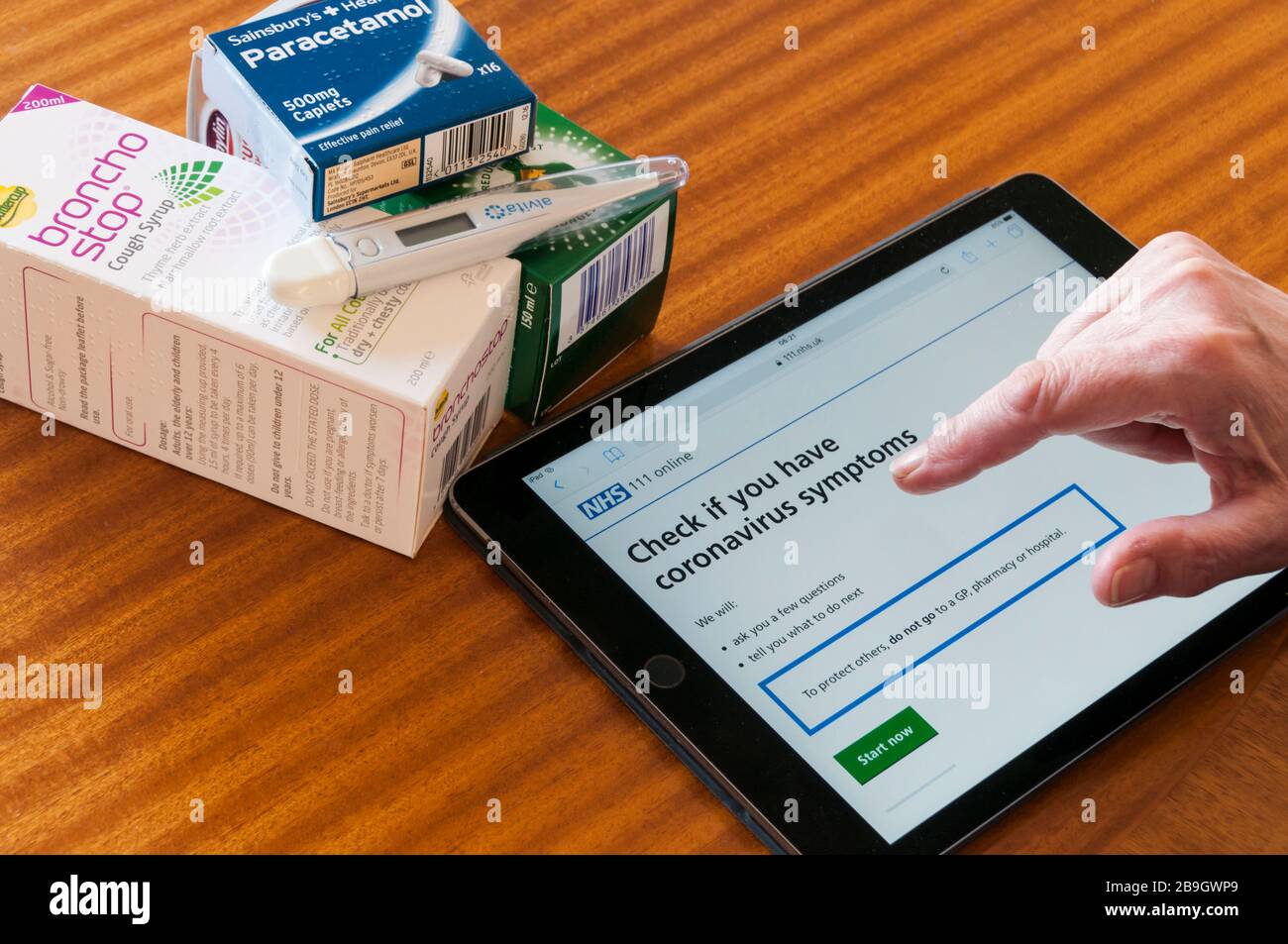 Una donna che utilizza un ipad per controllare il sito web NHS per consigli sui simpton Coronavirus Covid-19. Con medicinali e termometro. Foto Stock