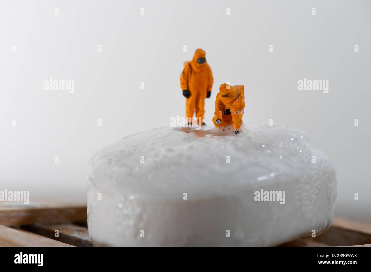 Immagine concettuale per Coronavirus con persone in miniatura su una barra di sapone in tute di nocciola test per la ricerca di batteri. Foto Stock