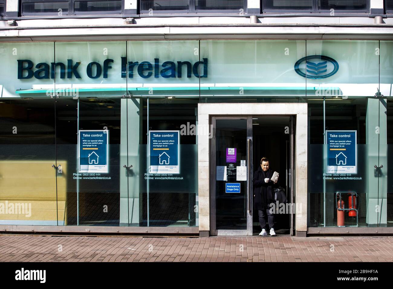 Una donna che lascia la filiale della Banca d'Irlanda su High Street a Belfast. Le banche sono state autorizzate a rimanere aperte in quanto sono considerate servizi essenziali. Foto Stock