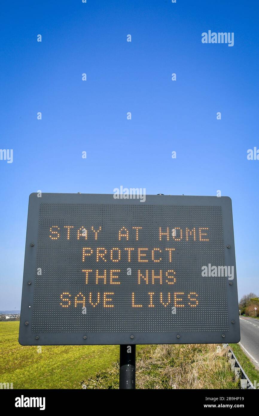 Un cartello stradale a matrice sulla A367 in Bath consiglia agli automobilisti di rimanere a casa per proteggere l'NHS e salvare vite il giorno dopo che il primo ministro Boris Johnson ha messo il Regno Unito in blocco per contribuire a frenare la diffusione del coronavirus. Foto Stock