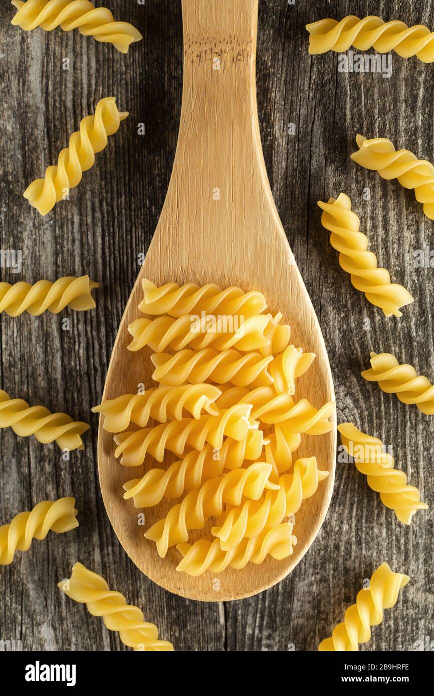 Fusilli pasta italiana sul cucchiaio di legno. La pasta a spirale su sfondo rustico. Da sopra Foto Stock