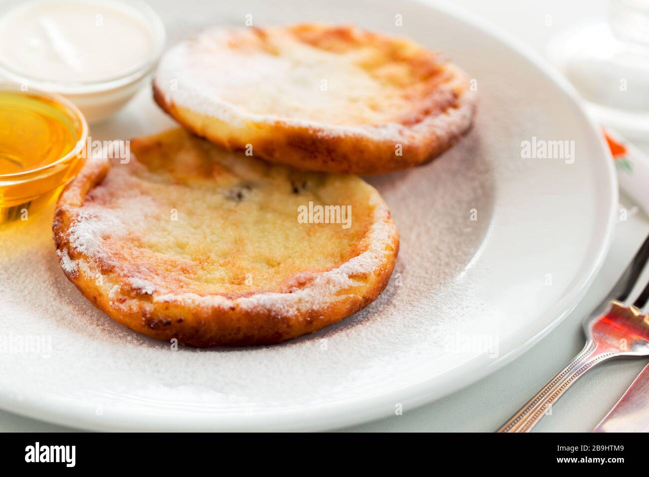 Cheesecake ucraini colazione con miele e crema su piatto bianco. Frittelle o frittelle di formaggio casolare Foto Stock