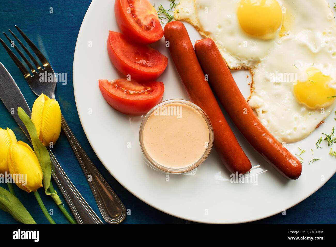 Le uova fritte con salsicce per la colazione si posano su fondo di legno blu Foto Stock