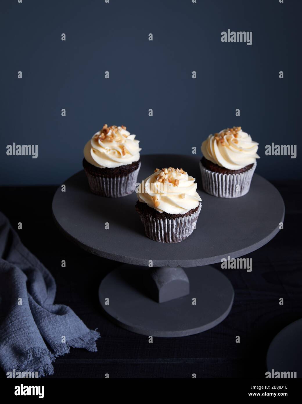 Cupcake al cioccolato con crema di burro bianco e arachidi su sfondo scuro con spazio libero per il testo Foto Stock