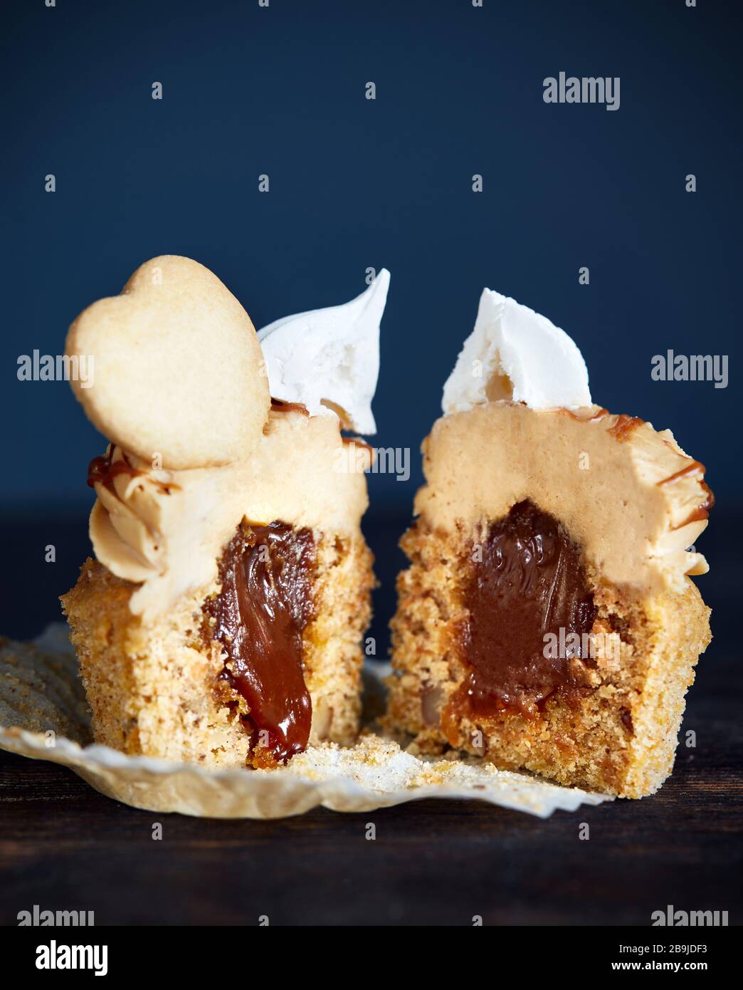 Taglio di cupcake di carota con caramello, noci e spezie decorate con biscotto a forma di cuore, meringa e caramello salato su sfondo scuro primo piano Foto Stock