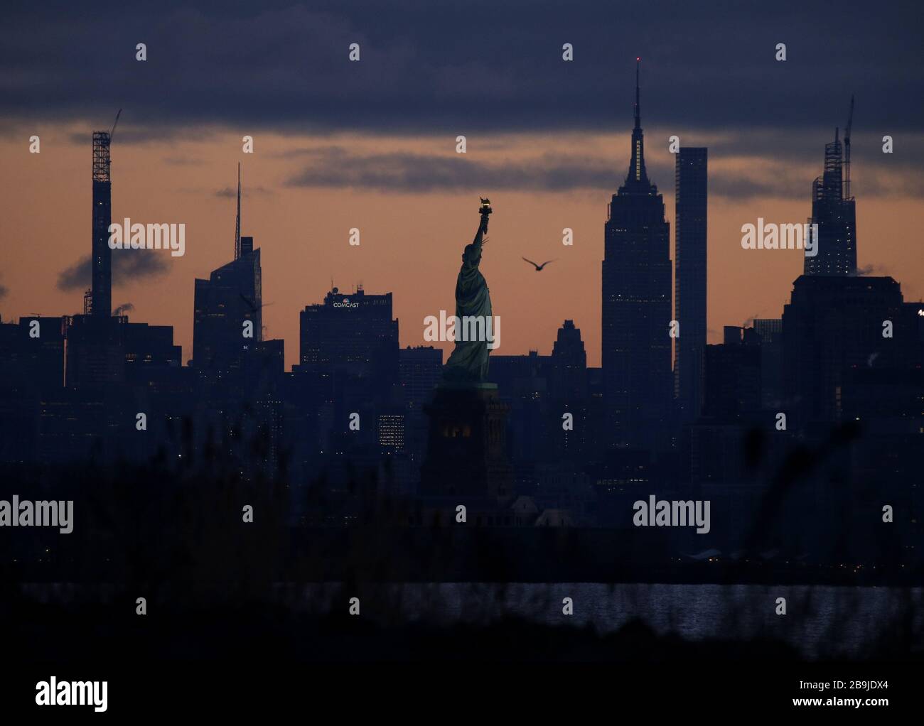 Il sole sorge sull'Empire state Building, la Statua della libertà e Manhattan a New York City martedì 24 marzo 2020. Il sindaco di New York, Bill de Blasio, ha affermato che il numero di casi positivi in città è stato di 13,119 alle 6 di lunedì. Foto di John Angelillo/UPI Foto Stock