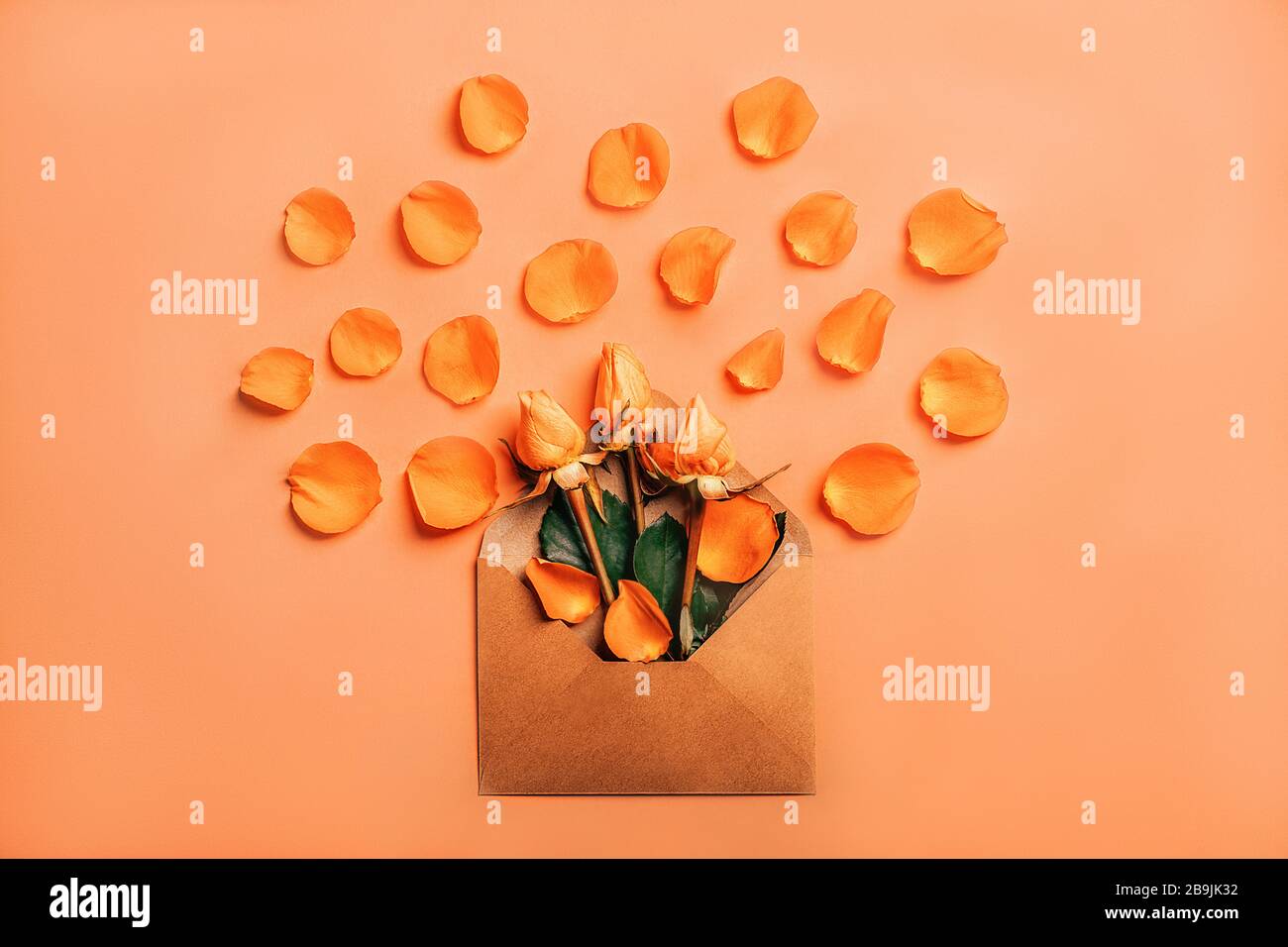 Busta di carta artigianale con rose arancioni in petali su sfondo corallino. Foto Stock