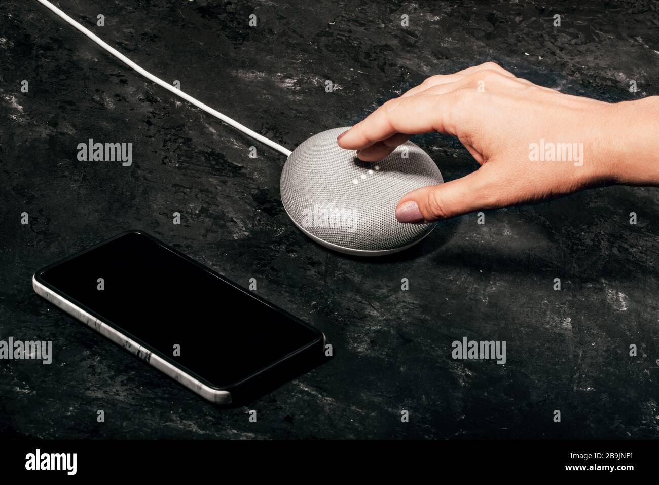 Concetto di Assistente digitale. Altoparlante intelligente da donna con luci LED attivate su un tavolo nero in cemento con smartphone. Foto Stock