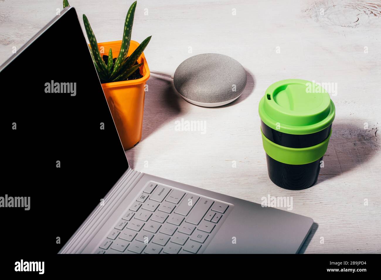 Concetto di Assistente digitale. Altoparlante intelligente con computer portatile, aloe vera pianta in vaso arancione e tazza da caffè riutilizzabile con coperchio verde su sfondo bianco. Foto Stock