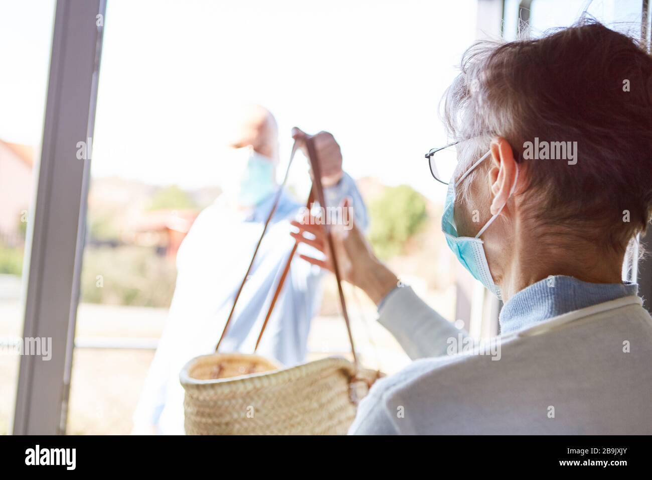 Donna anziana in quarantena con maschera facciale ottiene la consegna del cibo a casa Foto Stock