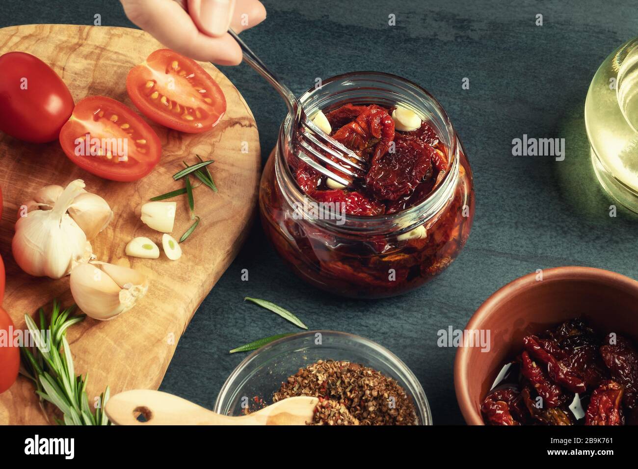 La mano femminile mette i pomodori a forcella in un vaso di vetro con una forchetta. Cottura di pomodori a base di spezie in scatola. Foto Stock