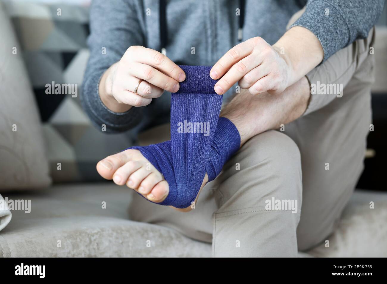 L'uomo si dà il primo aiuto che arrotola nastro di bendaggio blu sopra il piede Foto Stock