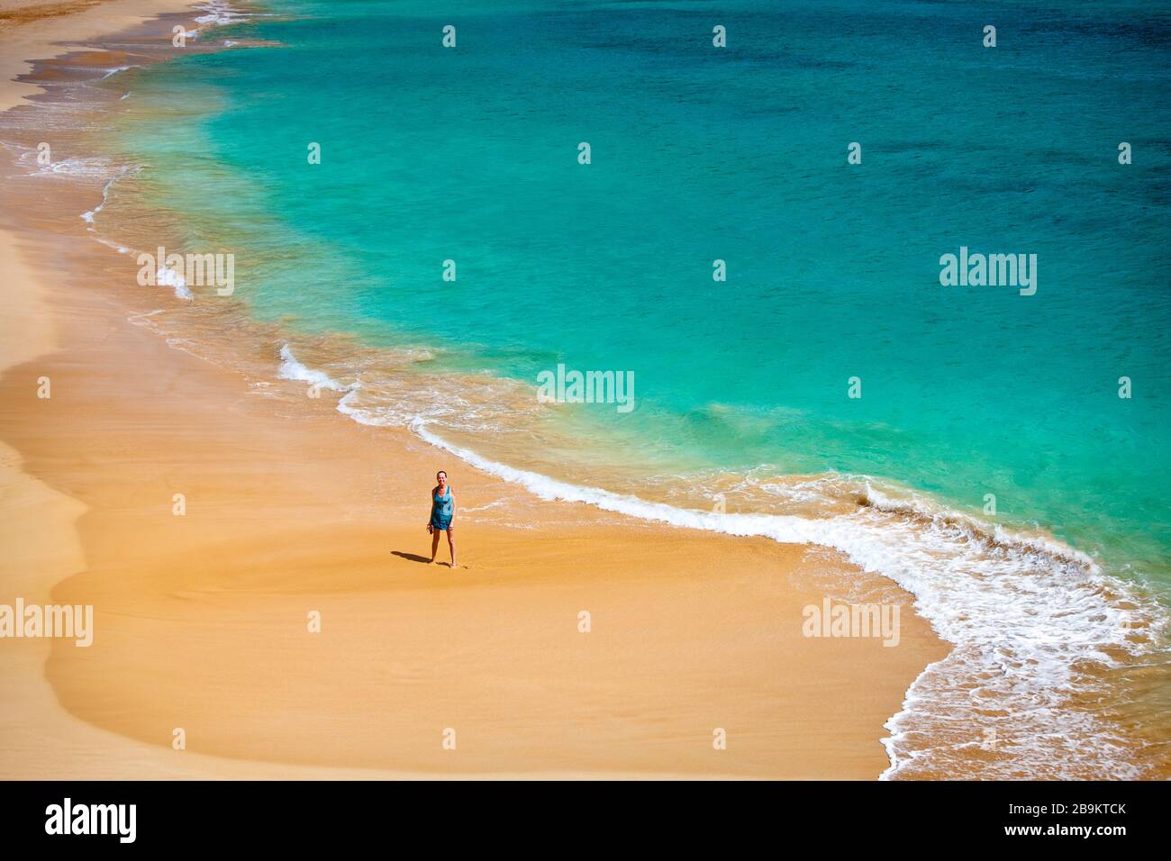Donna che cammina lungo una spiaggia tropicale al sole. Foto Stock