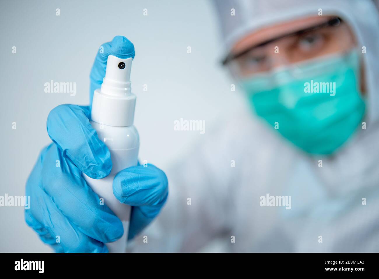 Il medico caucasico in una tuta protettiva e maschera chirurgica usare disinfettante per Coronavirus. Mani maschili che trattengono un gel antibatterico. Misure preventive ag Foto Stock