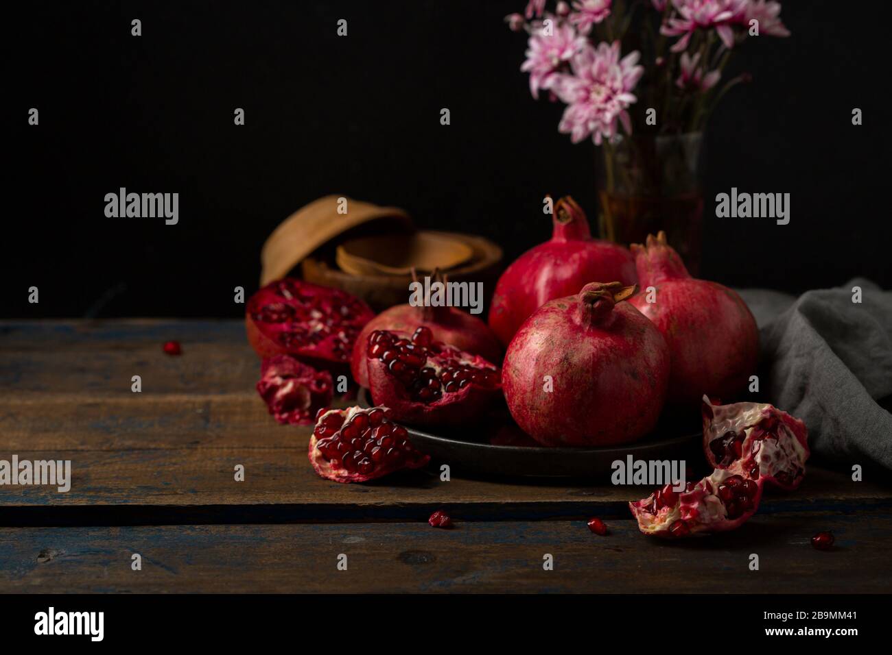 Diversi melograni su piatto su piatto di legno e fiori Foto Stock