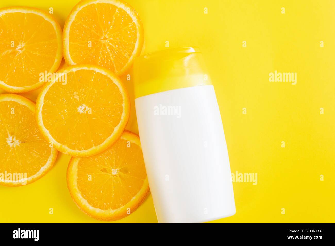 Crema solare su sfondo giallo con fette di arancione. Mock-up cosmetico di prodotti di bellezza per crema idratante, lozione, siero o olio essenziale. Vista dall'alto. Foto Stock