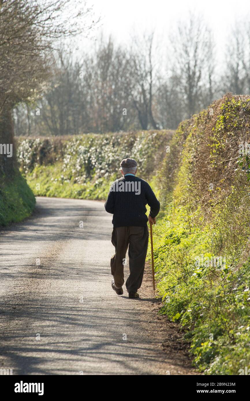 Un uomo fuori a piedi lungo una corsia di paese la mattina dopo che il primo ministro britannico Boris Johnson ha annunciato le restrizioni per contrastare la minaccia da parte del Co Foto Stock