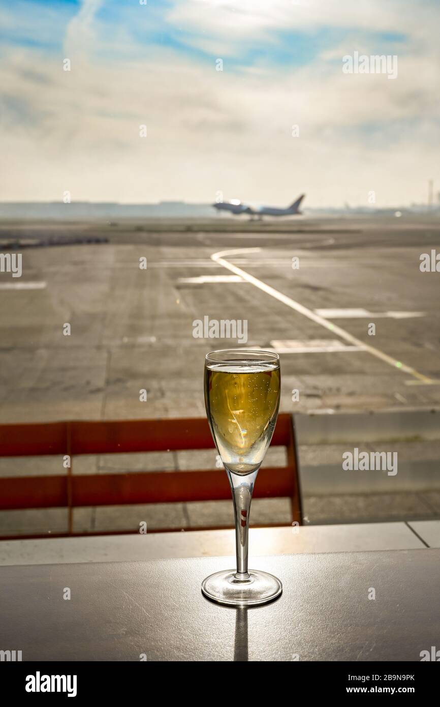 Bicchiere di champagne al tavolo in una business lounge dell'aeroporto con un aereo che decollo burred sullo sfondo Foto Stock