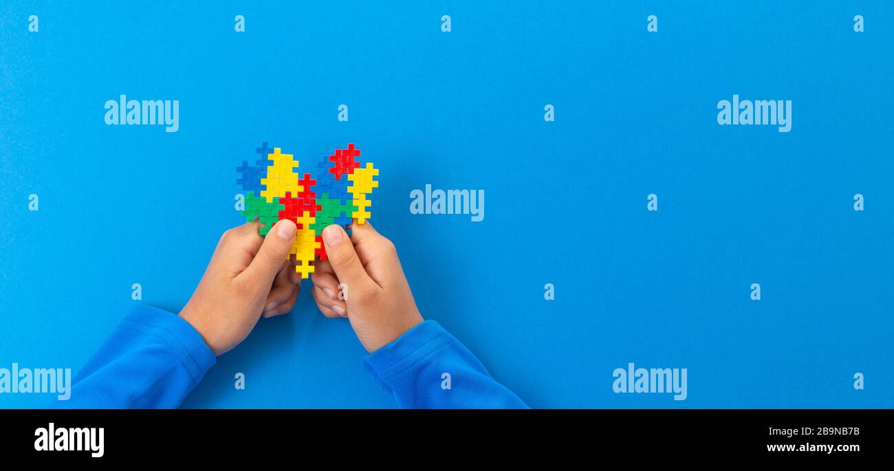 Concetto del giorno di consapevolezza di autismo del mondo. Le mani del bambino tengono il cuore colorato del puzzle su sfondo blu Foto Stock
