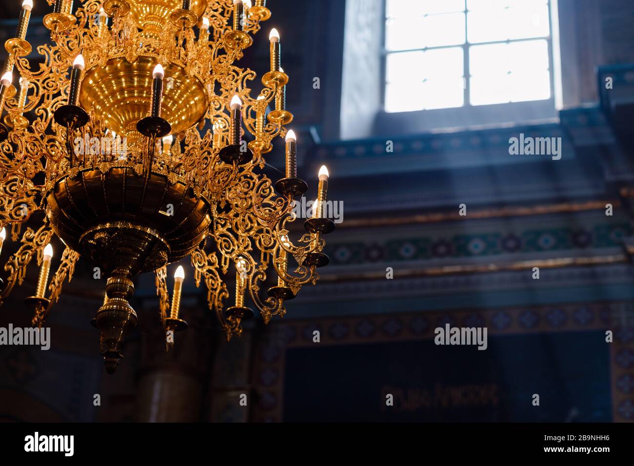 Grande lampadario in bronzo con candele elettriche nella chiesa cristiana cattedrale. Luce naturale dalla finestra della chiesa. Fuoco selettivo Foto Stock